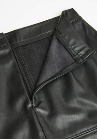 Czarna spódnica z sztucznej skóry z zamkiem błyskawicznym, o gładkiej fakturze i wewnętrznej podszewce, która wydaje się miękka i lekko puszysta.