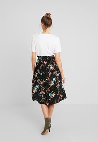 Zwarte midi-rok met bloemenmotief in verschillende kleuren. Gecombineerd met een wit T-shirt en olijfgroene enkellaarsjes. Losse, gerimpelde tailleband.