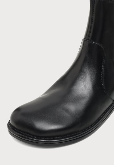 Gros plan d'une bottine en cuir noir lisse avec bout arrondi et couture visible le long du bord de la semelle.