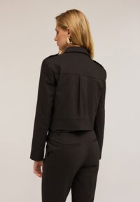 Sort cropped jakke med struktureret design, der har skuldertabs, en rygslids og en skræddersyet pasform. Glat, struktureret stof.