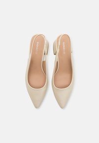 Beige színekben kapható, hegyes orrú, slingback magassarkú, sima szintetikus anyagból készült, alacsony blokk sarkú, és oldalt kivágott, a lábat felfedő dizájnnal. A márka logója belül látható.
