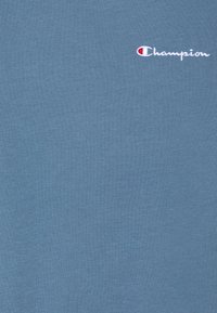 Blå bomull t-shirt med rund hals och korta ärmar. Har en liten broderad "Champion"-logga i vitt och rött på framsidan.