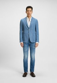 Ljusblå blazer med en texturerad tyg, två framfickor och knappar. Matchad med en vit skjorta och åtsittande blå jeans. Mörkbruna skor.