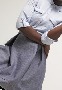 Camisa de color azul claro con cuello y botones, y dos bolsillos en el pecho; combinada con una falda gris con pliegues, que presenta una textura sutil y una silueta acampanada.