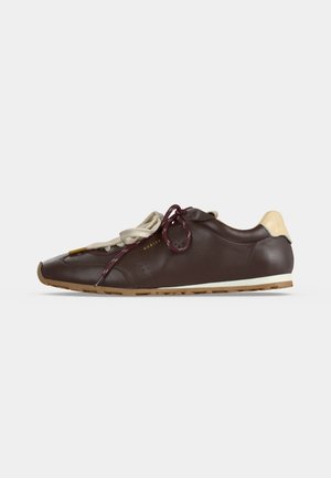 Vue de profil d’une basket en cuir marron foncé, avec des lacets crème et bordeaux, un empiècement clair au talon et une semelle couleur gomme.