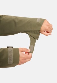 Olijfgroene jas  mouw met een klittenbandsluiting. De stof is glad, met een nette afwerking en een functie voor verstelbare strakkigheid bij de manchet.
