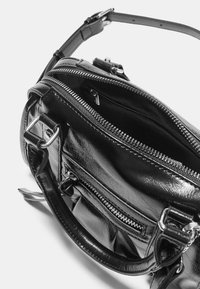 Czarna skórzana torebka o błyszczącej fakturze, z zamykanymi na zamek komorami, srebrnymi elementami i regulowanym paskiem. Widok wnętrza z góry.