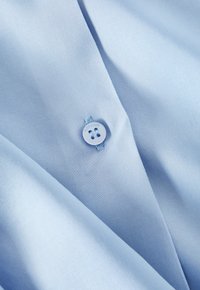 Velluto azzurro chiaro con una superficie liscia, con un pulsante bianco vicino al centro su cui è inciso la parola "TRIUM".