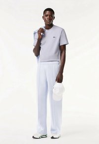 Gaiši zils īsroku krekls un atbilstoši bikses, izgatavotas no mīksta auduma. Modelis tur baltu cepuri un valkā baltas sporta kurpes ar zaļiem akcentiem.