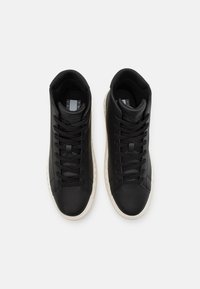 Ett par svarta högre sneakers med svarta snören och vita sulor, sedd uppifrån på en vit bakgrund.