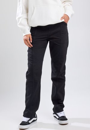 Black denim pants with a straight leg design, featuring front pockets and visible stitching details. Paired with black and white sneakers.