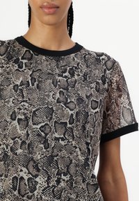 Hieno lyhythihainen toppi, jossa on käärmeennahkakuosi beige- ja mustana, mustalla pyöreällä kaula-aukkolla ja käännetyillä hihoilla.