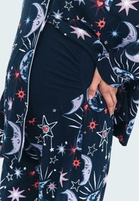 Marinblå pyjamasset med himmelskt tryck som har månar, stjärnor och hjärtan. Mjuk material, avslappnad passform och skjorta med knappstängning och kontrasterande kant.