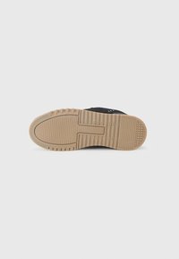 Black sneaker with a textured upper, featuring a gum rubber outsole. The sole has a patterned tread for grip and durability.