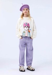 Sudadera crema con un gráfico de un gato con un sombrero rosa, combinada con pantalones lavanda y sandalias en blanco y negro. Boina de punto morada en la cabeza.