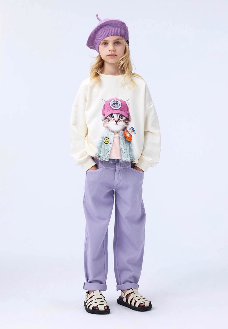 Sudadera crema con un gráfico de un gato con un sombrero rosa, combinada con pantalones lavanda y sandalias en blanco y negro. Boina de punto morada en la cabeza.