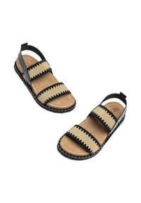 Tan sandalen met zwarte zigzagpatronen op de bandjes en een grijze achterband. Voorzien van een gestructureerde voetbed en een zwart, gespikkeld zool.