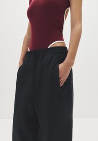Bordeaux kleurige bodysuit met witte accenten, gecombineerd met zwarte, losse broek met een elastische tailleband en zijzakken.