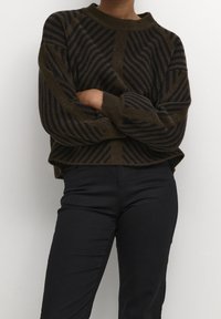 Maglione a righe marrone e blu navy in maglia, con scollatura a girocollo a costine, vestibilità ampia e spalle cadenti. Indossato con pantaloni neri.