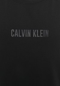 Czarny bawełniany t-shirt z okrągłym dekoltem. Na przodzie wyróżnia się mocny, metaliczny napis "CALVIN KLEIN" w delikatnym gradiencie. Gładka tekstura.