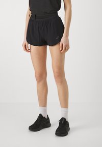 Shorts sportivi neri con vita elastica, caratterizzati da un piccolo logo e da un materiale leggero e traspirante. Abbinati a scarpe da corsa nere e calze bianche.
