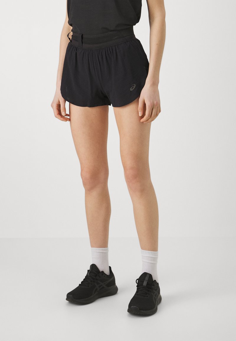 Shorts sportivi neri con vita elastica, caratterizzati da un piccolo logo e da un materiale leggero e traspirante. Abbinati a scarpe da corsa nere e calze bianche.