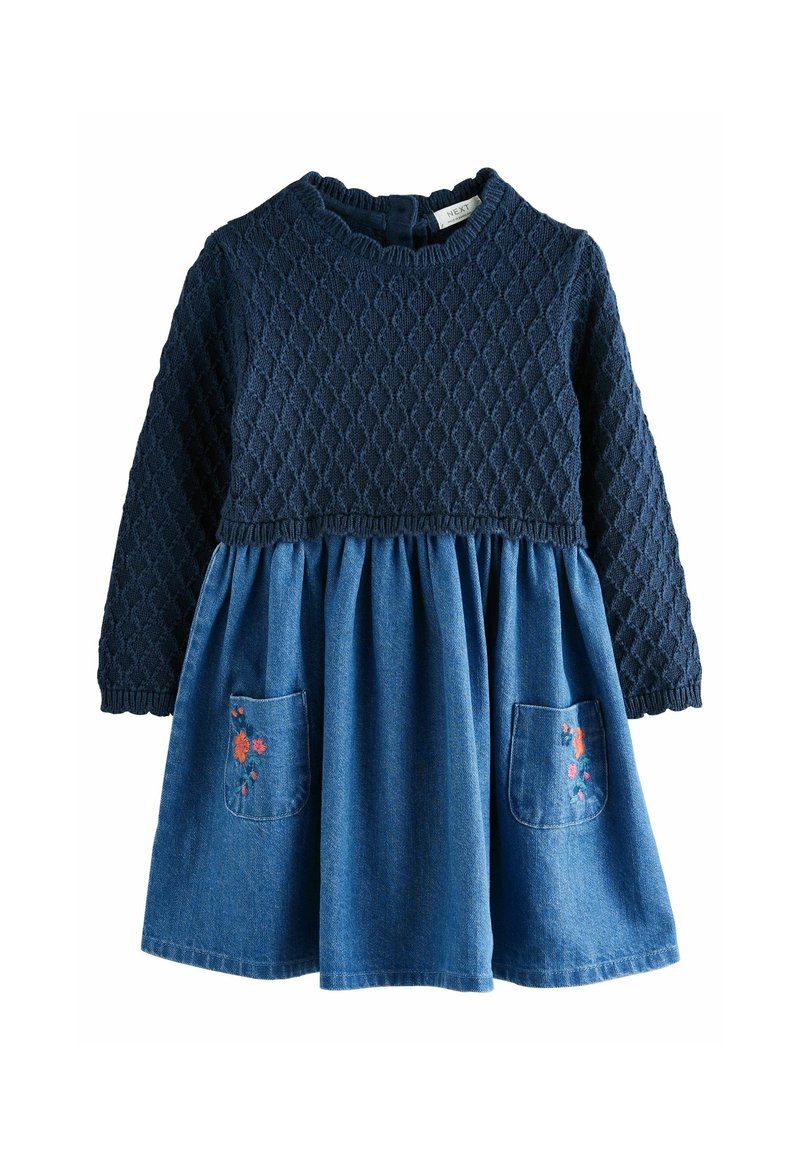 Top à manches longues en maille texturée bleu marine avec une robe jupe en denim bleu, comportant deux poches avant brodées de fleurs orange et roses.