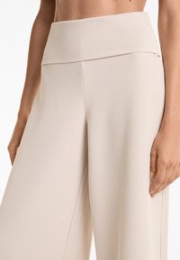 Lichtbeige wijdvallende broek gemaakt van ribbelstof, met een hoog model en een gladde textuur, en met tailleursteken langs de pijpen.