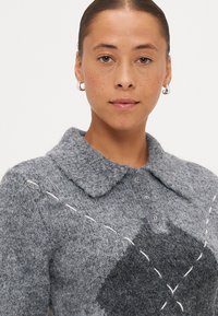 Gray wool sweater with a collared neckline, featuring three buttons and contrasting stitching. Distinct geometric pattern in dark gray.