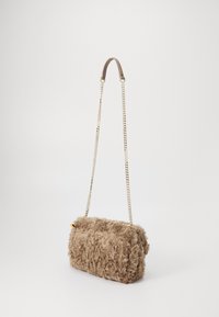 Kleine rechthoekige beige fluffy handtas met gouden kettingriem en een korte gewatteerde leren handgreep tegen een lichte achtergrond.