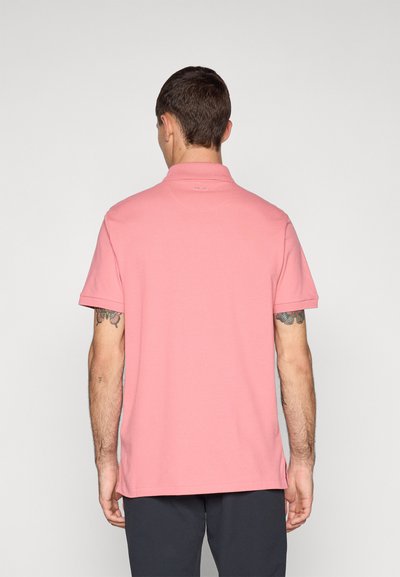 Camisa polo de manga curta, cor rosa claro, feita de tecido suave. Apresenta um colarinho clássico e um pequeno logotipo na parte de trás do pescoço.