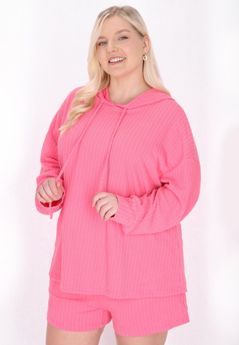Felpa rosa con cappuccio, caratterizzata da una texture a coste e maniche lunghe, abbinata a pantaloni corti coordinati, entrambi con una vestibilità comoda e dettagli con cordino.