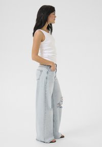 Top sin mangas blanco combinado con jeans de pierna ancha azul claro con detalles desgastados. El conjunto tiene un ajuste casual y una textura suave.
