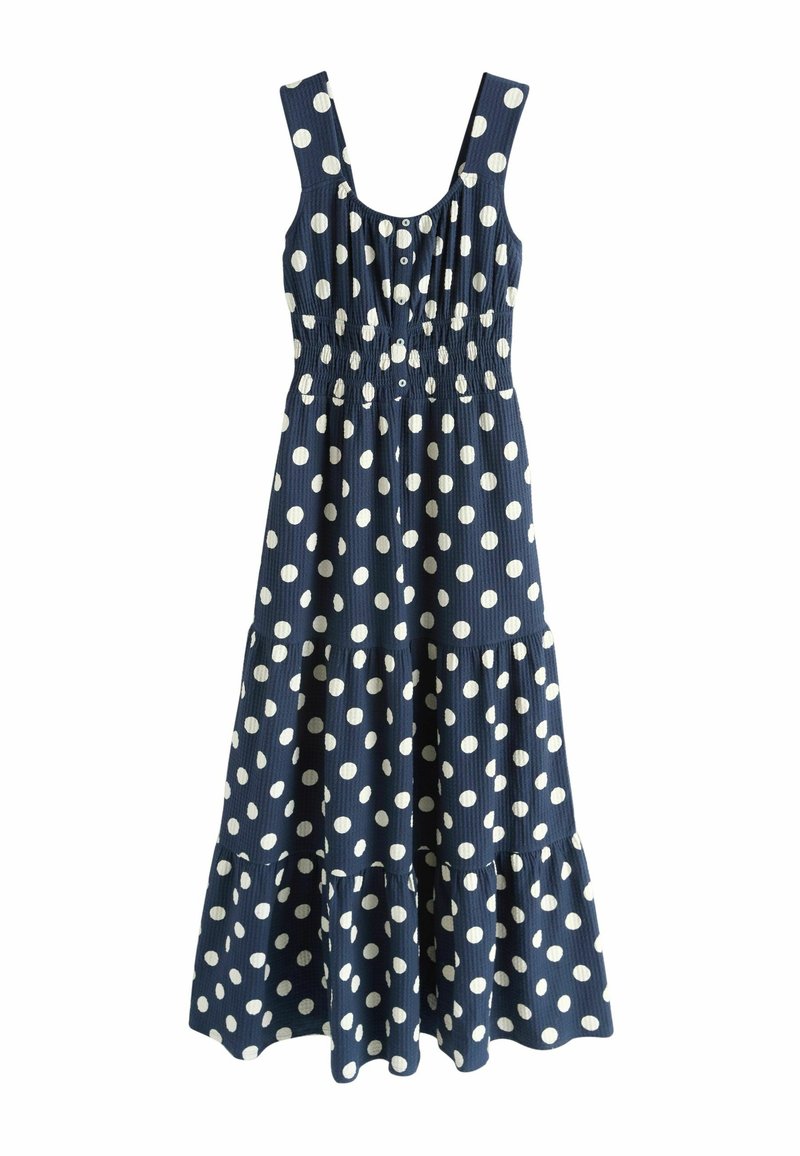Robe sans manches bleu marine à gros pois blancs, boutonnée sur le devant, taille froncée et jupe évasée à volants.