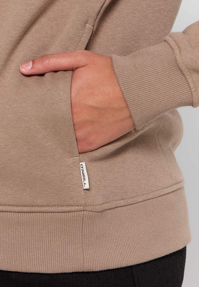 Felpa marrone chiaro con texture a coste, dotata di una tasca laterale e di un piccolo etichetta del marchio vicino all'orlo. Il design è casual e aderente.