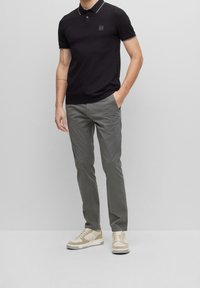 Czarny polo z dopasowanym krojem, krótkimi rękawami, kontrastującymi wykończeniami, w połączeniu z jasnoszarymi spodniami i beżowymi trampkami. Zawiera detal z logo.