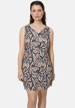 Mujer con un vestido sin mangas de longitud hasta la rodilla con un patrón geométrico abstracto en beige, marrón y azul marino sobre fondo blanco.