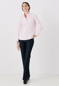 Camisa de botón rosa claro con cuello puntiagudo, combinada con jeans de pierna recta azul oscuro y zapatos de tacón negros.