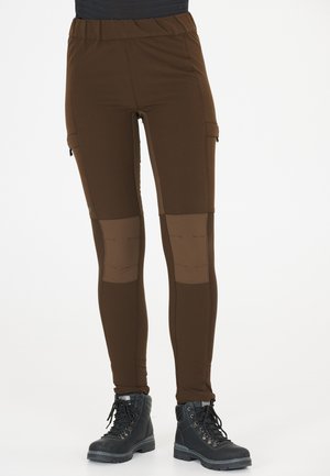 Braune enganliegende Hose mit einem elastischen Bund und Kniepatches. Sie verfügt über Seitentaschen und ist aus einem glatten, dehnbaren Stoff gefertigt. Getragene schwarze Stiefel.