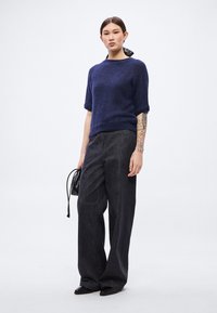 Πλεκτό πουλόβερ σε ναυτικό μπλε με κοντά μανίκια, άνετο σκούρο τζιν παντελόνι, μαύρα επίπεδα παπούτσια και μικρή μαύρη τσάντα χειρός.