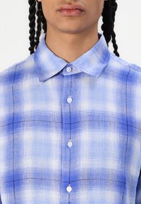 Lightweight blue plaid button-up shirt featuring a collared neckline, white buttons, and contrasting black stitching on the fabric.