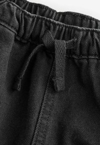 Ceinture en tissu noir avec une garniture élastique et un cordon de serrage. La texture est lisse avec un léger éclat, mettant en valeur les détails de couture.