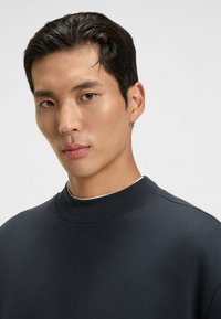 Navy mock neck sweatshirt made of smooth fabric with a fitted collar and a minimalistic design. Features a subtle sheen and stitch detailing.