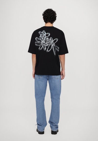 Μαύρο oversized t-shirt με γυαλιστερό floral σχέδιο στην πλάτη. Συνδυάζεται με ανοιχτό μπλε τζιν και μαύρα παπούτσια.