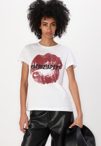 Maglietta bianca in cotone con una grande stampa di rossetto rosso e la scritta "PATRIZIA PEPE" in grassetto nero, abbinata a pantaloni in ecopelle nera.