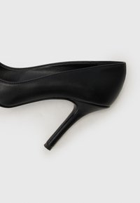 Fekete bőr magassarkú cipő sima textúrával és hegyes orral. Karcsú stiletto sarokkal és minimalista dizájnnal rendelkezik.