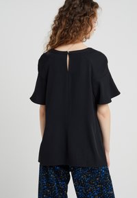 Czarny krótki top z krótkim rękawem wykonany z gładkiego materiału, z okrągłym dekoltem i detalem w kształcie otworu z tyłu. Ma luźny krój.