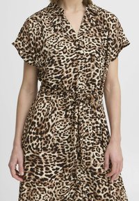 Leopardmönstrad klänning i mjukt tyg med korta ärmar, krage och midjebälte. Har bruna och beige nyanser i ett djärvt mönster.