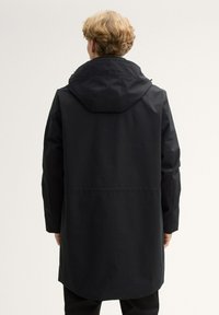 Must mustem coat kapuutsiga, pikk disain, esiseamse detail ja veidi kaardus äärega. Siidine tekstuur ja minimalismistiil.