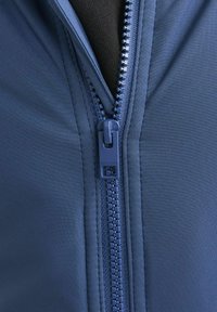Marinblå zip-up jacka med en slät tygkonstruktion, kraftig dragkedja med en logotypförsedd dragtab och synliga sömmar längs kanterna.